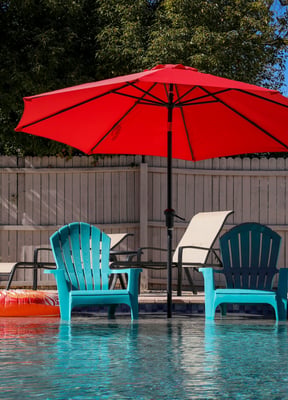 Sunny backyard pool with teal chairs and red umbrella