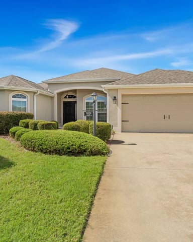Large white stucco home with red front door, arched windows, manicured hedges, and a black lifted golf cart in the driveway
