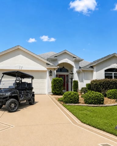 White house with large black golf cart parked in driveway, surrounded by green lawn and mature trees